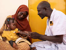 En av RESCUE:s medarbetare ger vård till en flicka som sitter i sin mammas knä. 